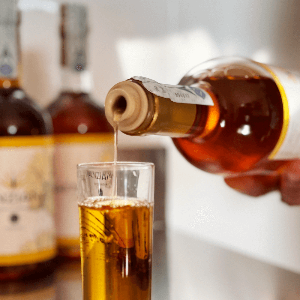 Bicchiere di vetro con liquore alla genziana mentre viene versato dalla bottiglia