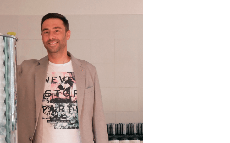 Ragazzo sorridente con t-shirt bianca e stampa fantasia con giacca grigia accanto ad una cisterna