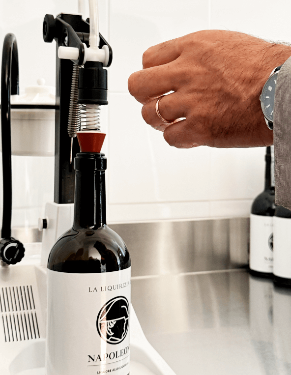 Bottiglia di liquirizia di Napoleone sotto la macchina per estrarre il liquore alla liquirizia con mano maschile che si avvicina a sistemarla