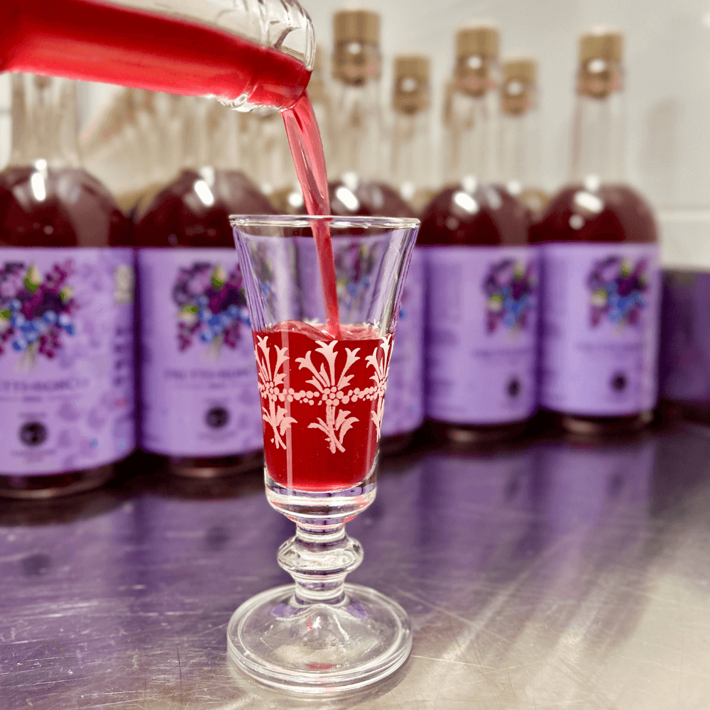 bicchierino di vetro che viene riempito di liquore rosso con bottiglie come sfondo