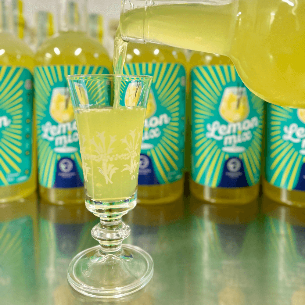 bicchierino di vetro che viene riempito di liquore giallo con bottiglie come sfondo