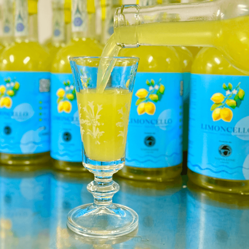 bicchierino di vetro che viene riempito di liquore limoncello giallo con bottiglie come sfondo